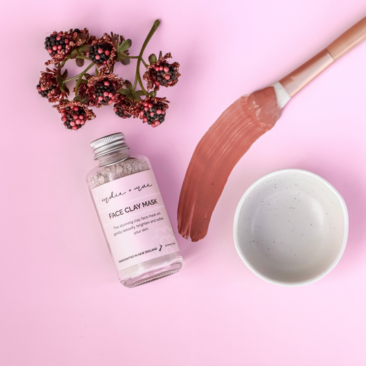 Face clay mask bottle with a brush and flowers on a pink background | Indie + Mae