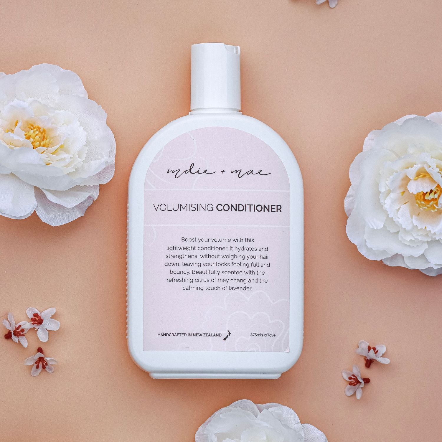 Volumising conditioner bottle with floral elements on a peach background | Indie + Mae