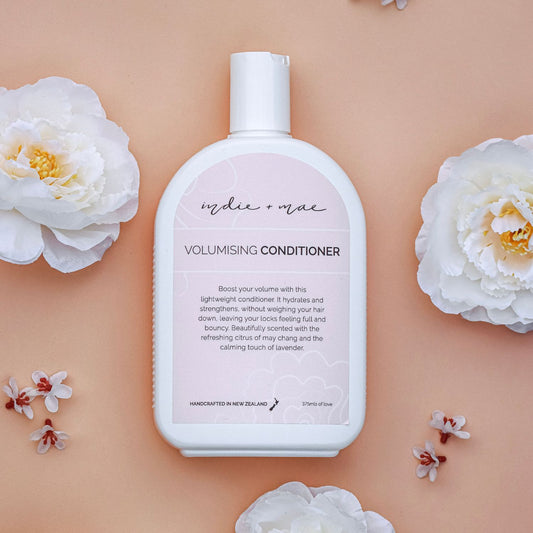 Volumising conditioner bottle with floral elements on a peach background | Indie + Mae