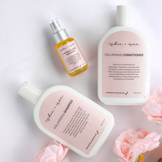 Two bottles of 'Indie & Mae' volumising shampoo and conditioner with pink flowers on a light background.