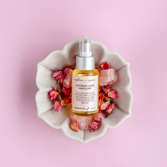 Hair elixir bottle in a decorative bowl with flowers on a pink background | Indie + Mae