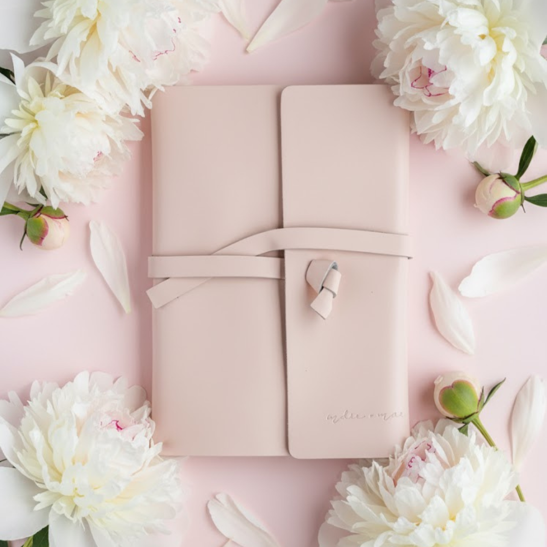Pink leather journal with a bow on a pink background with white flowers | Indie + Mae | Gifts Under $50